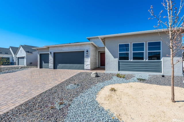 view of front of property featuring a garage, stone siding, decorative driveway, and stucco siding