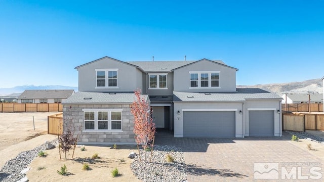 traditional-style home featuring decorative driveway, stucco siding, an attached garage, a mountain view, and fence