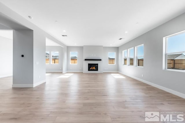 unfurnished living room with a glass covered fireplace, light wood-style flooring, baseboards, and recessed lighting