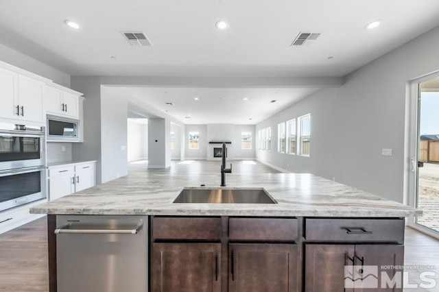 kitchen with a sink, visible vents, open floor plan, built in microwave, and a center island with sink