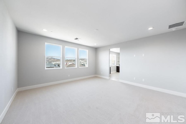 empty room with baseboards, visible vents, and light colored carpet