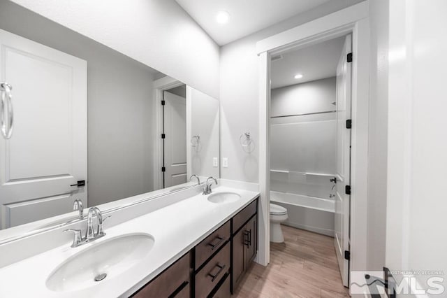 bathroom featuring wood finished floors, a sink, toilet, and double vanity