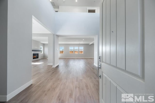 entrance foyer with light wood-type flooring, a warm lit fireplace, and baseboards