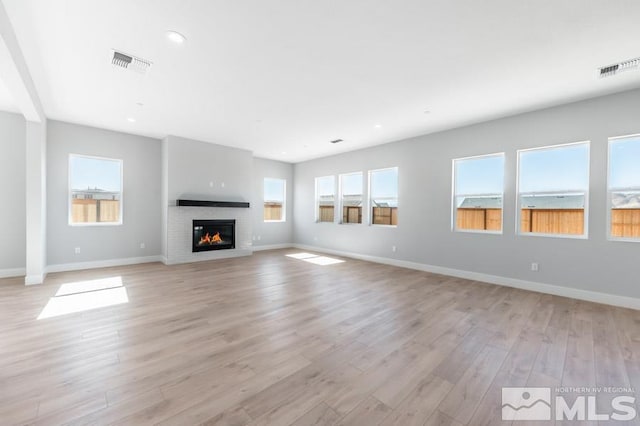 unfurnished living room with light wood-style floors, a glass covered fireplace, visible vents, and baseboards