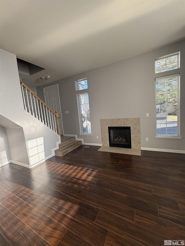 unfurnished living room with a wealth of natural light, stairway, a tile fireplace, and wood finished floors