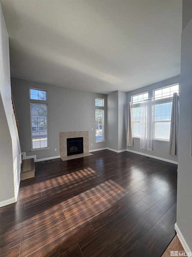 unfurnished living room featuring dark wood-style floors, baseboards, visible vents, and a tiled fireplace