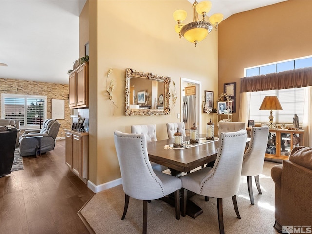 dining room with dark wood-style floors, high vaulted ceiling, an inviting chandelier, and baseboards