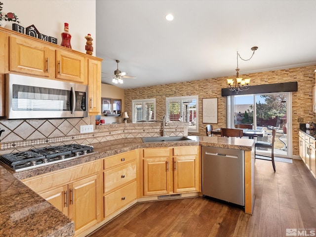 kitchen with stainless steel appliances, tile counters, dark wood-type flooring, a sink, and a peninsula