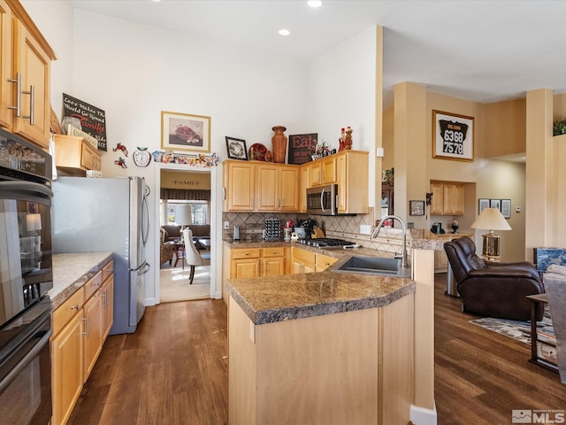 kitchen featuring a peninsula, a sink, open floor plan, appliances with stainless steel finishes, and light brown cabinetry