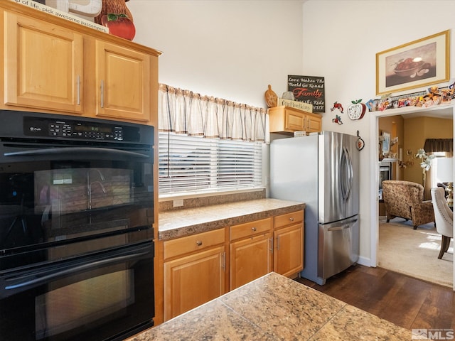 kitchen with tile countertops, dobule oven black, light brown cabinetry, dark wood-type flooring, and freestanding refrigerator