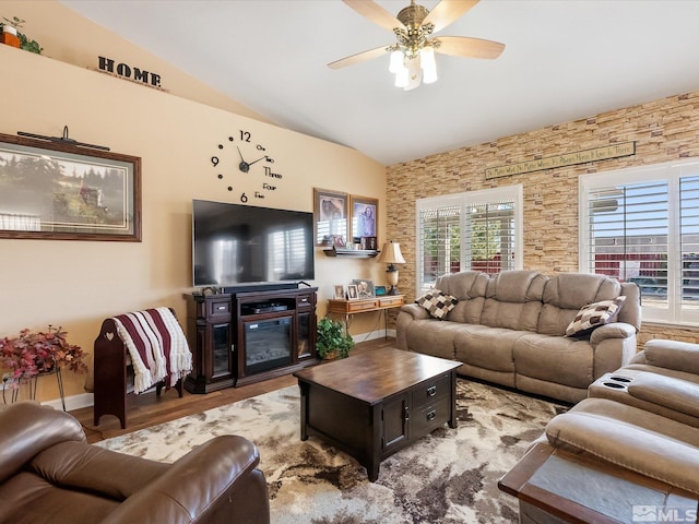 living area with lofted ceiling, a glass covered fireplace, ceiling fan, and wood finished floors