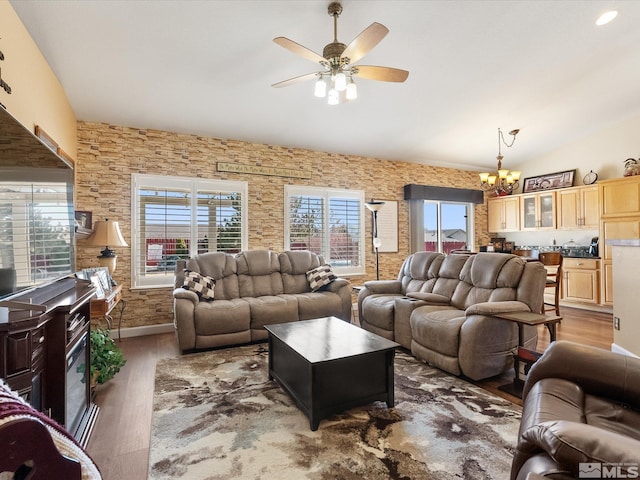 living area with ceiling fan with notable chandelier, lofted ceiling, and wood finished floors