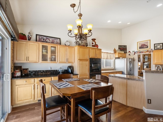 kitchen featuring dobule oven black, dark wood-style flooring, freestanding refrigerator, light brown cabinetry, and a notable chandelier