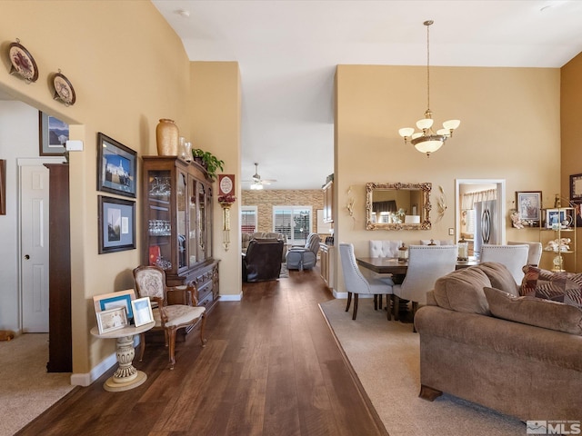 living room featuring ceiling fan with notable chandelier, a high ceiling, dark wood-style flooring, and baseboards