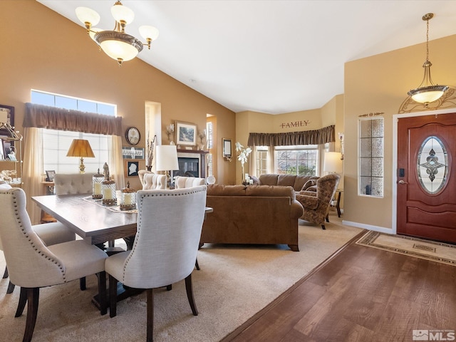 dining space with baseboards, high vaulted ceiling, wood finished floors, and a glass covered fireplace