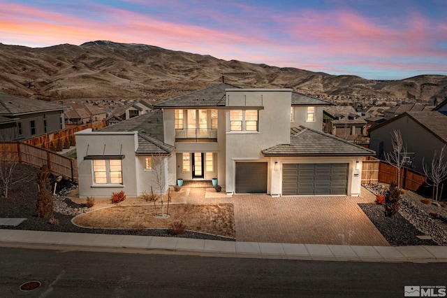 view of front of property featuring decorative driveway, stucco siding, a mountain view, fence, and a garage