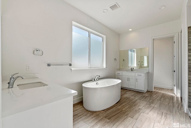 bathroom with a soaking tub, visible vents, two vanities, and a sink