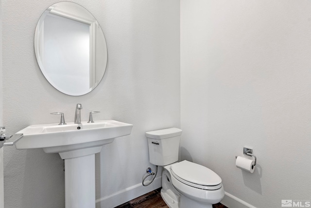 bathroom with toilet, a sink, baseboards, and wood finished floors