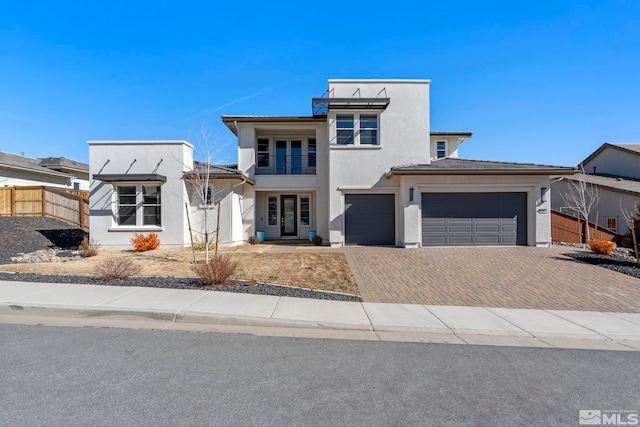 view of front of house with a balcony, a garage, fence, decorative driveway, and stucco siding