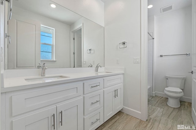 bathroom with double vanity, visible vents, toilet, a sink, and baseboards