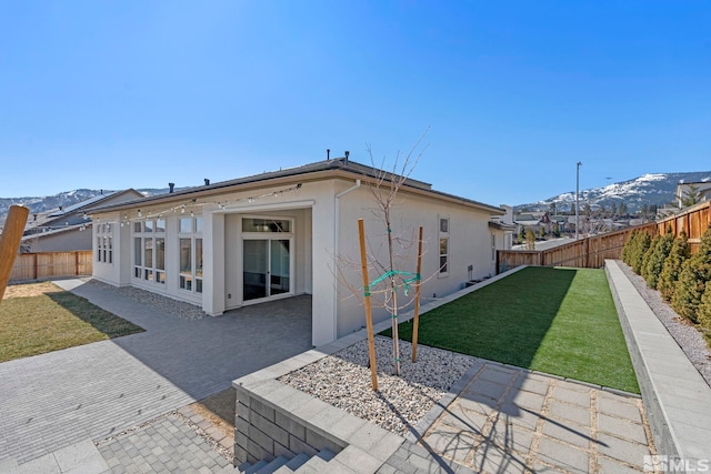 rear view of property with a lawn, a fenced backyard, a patio area, a mountain view, and stucco siding