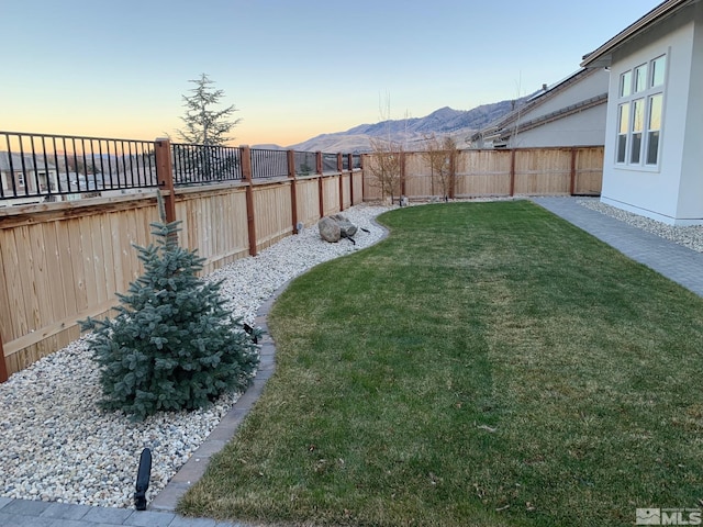 yard at dusk featuring a fenced backyard and a mountain view