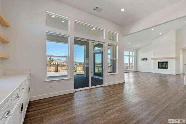 unfurnished living room with dark wood-type flooring, visible vents, a fireplace, and baseboards