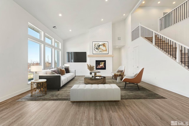 living room with a large fireplace, wood finished floors, stairs, and baseboards