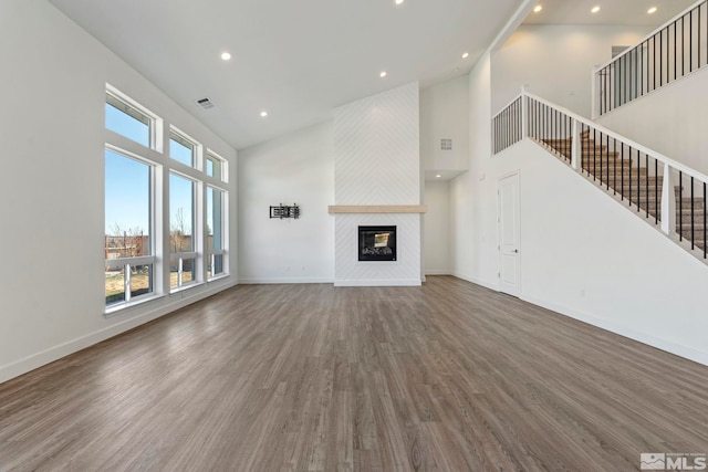 unfurnished living room with a large fireplace, wood finished floors, a towering ceiling, baseboards, and stairs