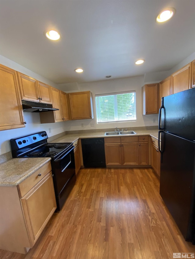 kitchen with a sink, under cabinet range hood, black appliances, and light wood finished floors