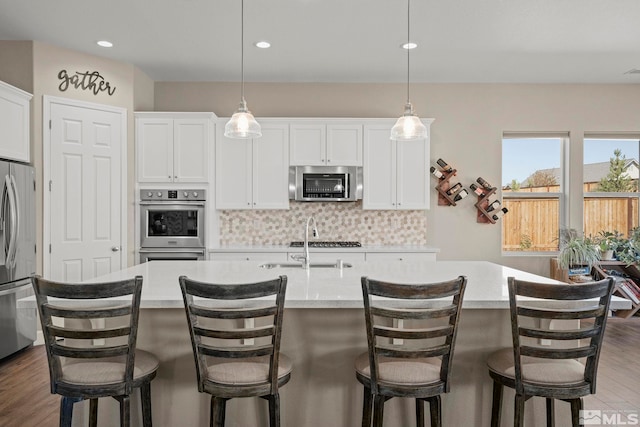 kitchen featuring a center island with sink, decorative backsplash, appliances with stainless steel finishes, wood finished floors, and light countertops