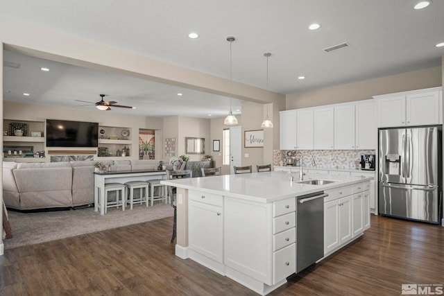 kitchen with stainless steel appliances, dark wood-style flooring, a sink, white cabinets, and a center island with sink