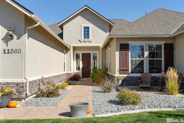 doorway to property featuring stone siding, roof with shingles, and stucco siding