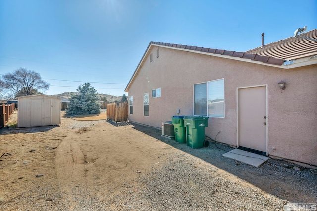 view of side of home featuring an outbuilding, a tile roof, stucco siding, fence, and a shed