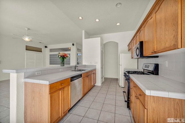 kitchen featuring tile countertops, light tile patterned floors, stainless steel appliances, a sink, and a peninsula