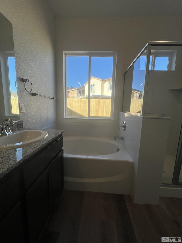 full bathroom with a textured wall, a garden tub, wood finished floors, vanity, and a stall shower