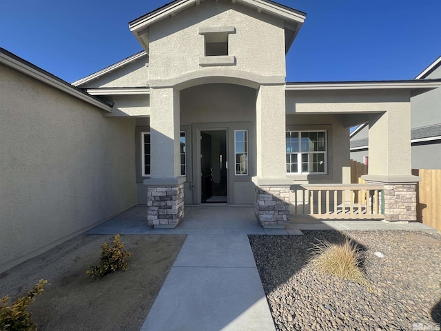 entrance to property with stone siding, covered porch, and stucco siding