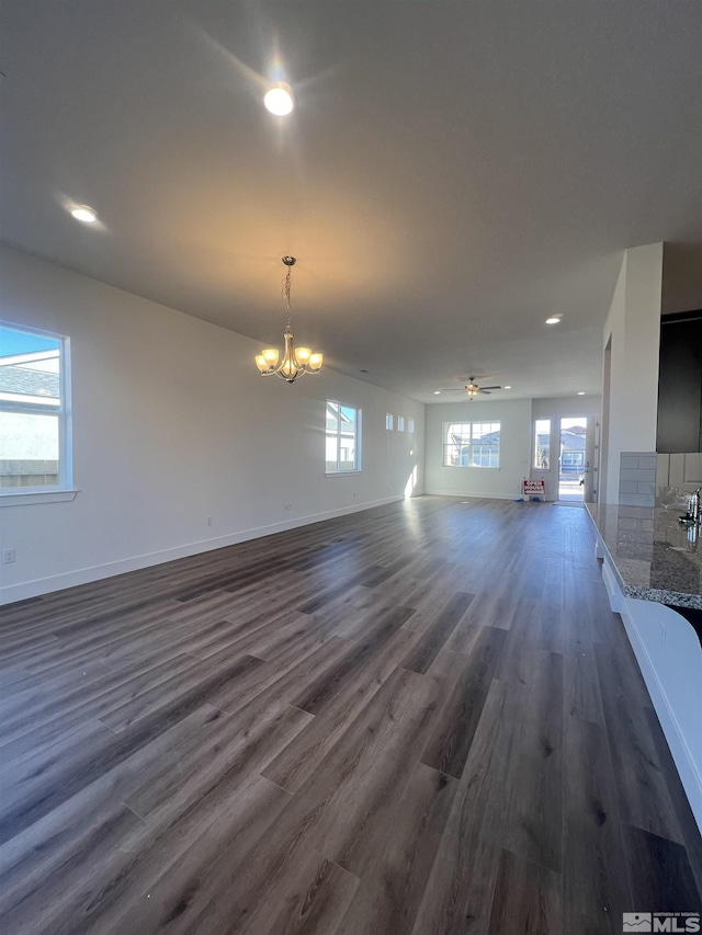 unfurnished living room featuring ceiling fan with notable chandelier, recessed lighting, dark wood finished floors, and baseboards