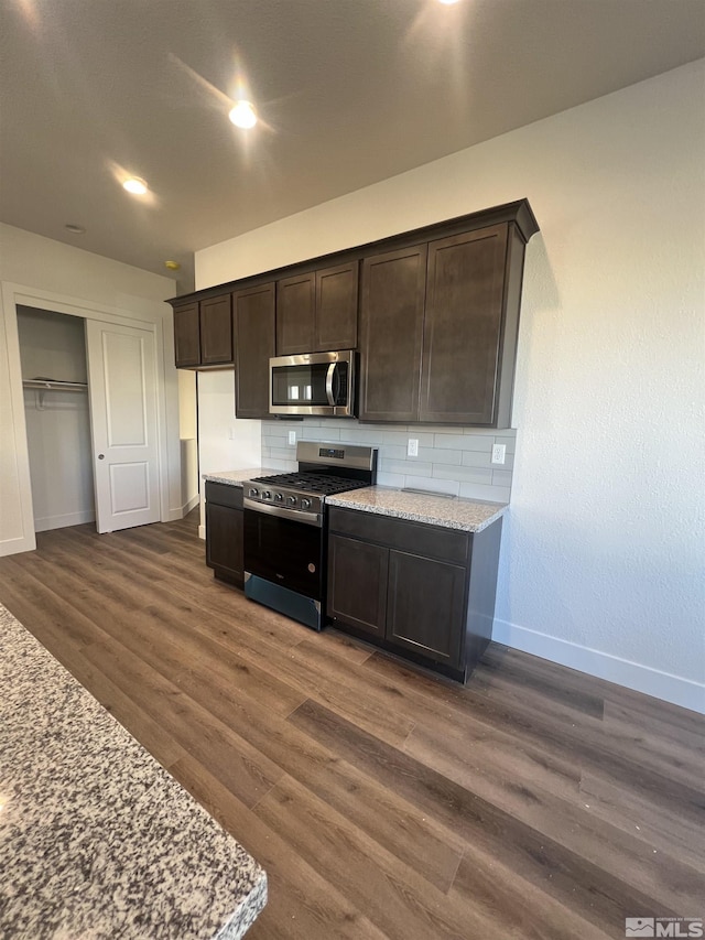 kitchen with appliances with stainless steel finishes, dark wood finished floors, dark brown cabinetry, and baseboards