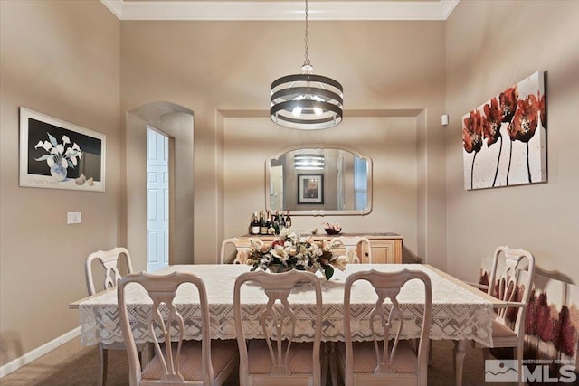 carpeted dining room with ornamental molding, arched walkways, baseboards, and an inviting chandelier