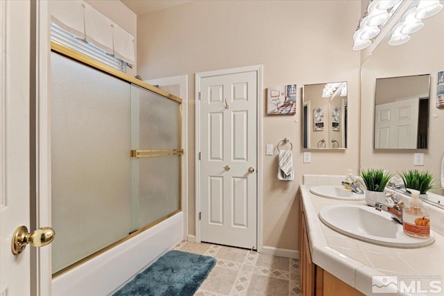 full bath with double vanity, enclosed tub / shower combo, baseboards, and a sink