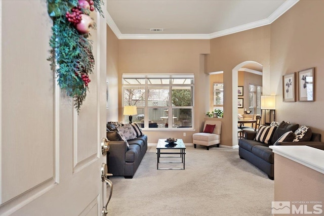 carpeted living area featuring ornamental molding, arched walkways, visible vents, and baseboards