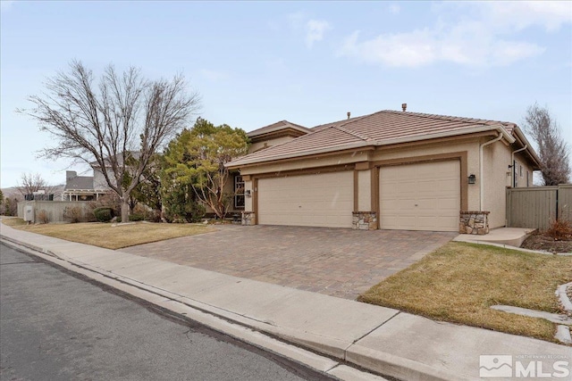 view of front of property featuring an attached garage, a tiled roof, stone siding, decorative driveway, and stucco siding