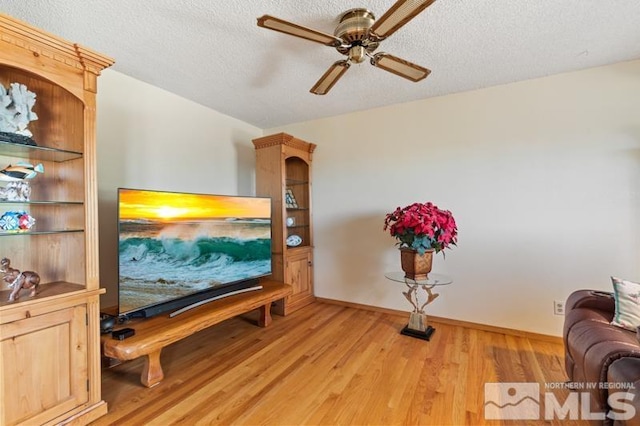 living room with a textured ceiling, light wood finished floors, a ceiling fan, and baseboards