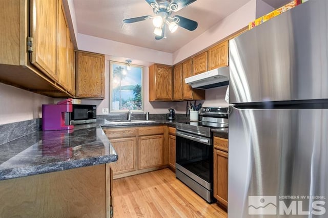 kitchen featuring light wood-style flooring, under cabinet range hood, stainless steel appliances, a sink, and brown cabinetry