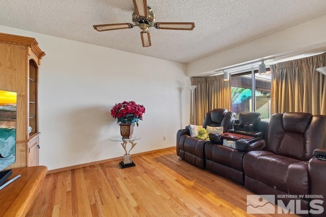 living room featuring light wood finished floors, baseboards, a ceiling fan, and a textured ceiling