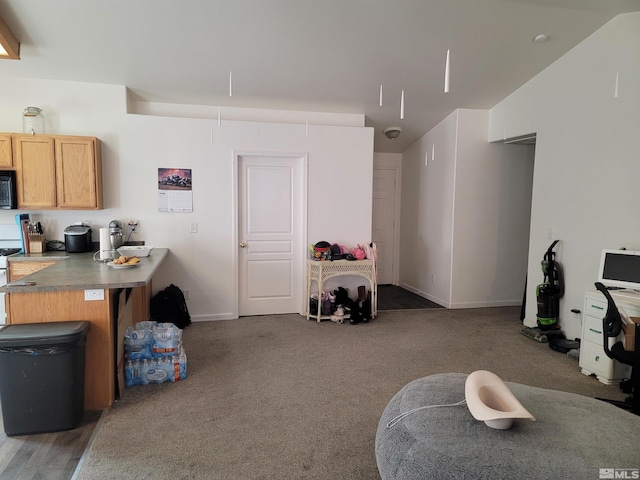 interior space featuring open floor plan, vaulted ceiling, light countertops, carpet floors, and black microwave