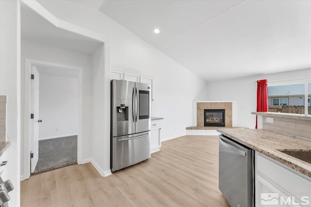 kitchen featuring light wood finished floors, white cabinets, a tile fireplace, appliances with stainless steel finishes, and vaulted ceiling