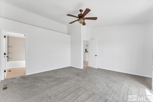 carpeted spare room featuring visible vents, vaulted ceiling, baseboards, and ceiling fan