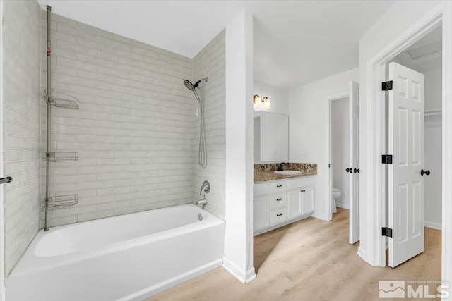 bathroom featuring toilet, vanity, shower / tub combination, wood finished floors, and baseboards